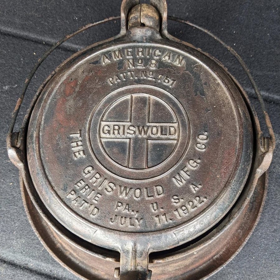 Close-up of a vintage cast iron waffle iron lid marked “Griswold MFG CO, Erie, PA, U.S.A., Pat’d July 11, 1922” with a circular logo and the number 8. The iron shows signs of age and wear.