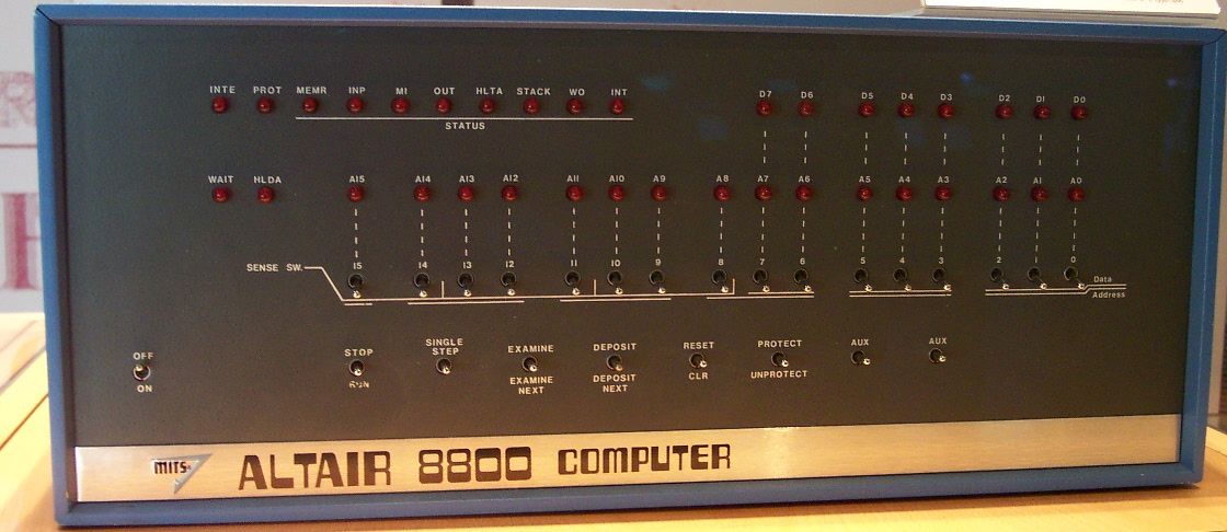 Front view of an Altair 8800 computer with switches, indicator lights, and labeled panels for input, status, and controls. The computer’s name is displayed on a metal strip at the bottom.