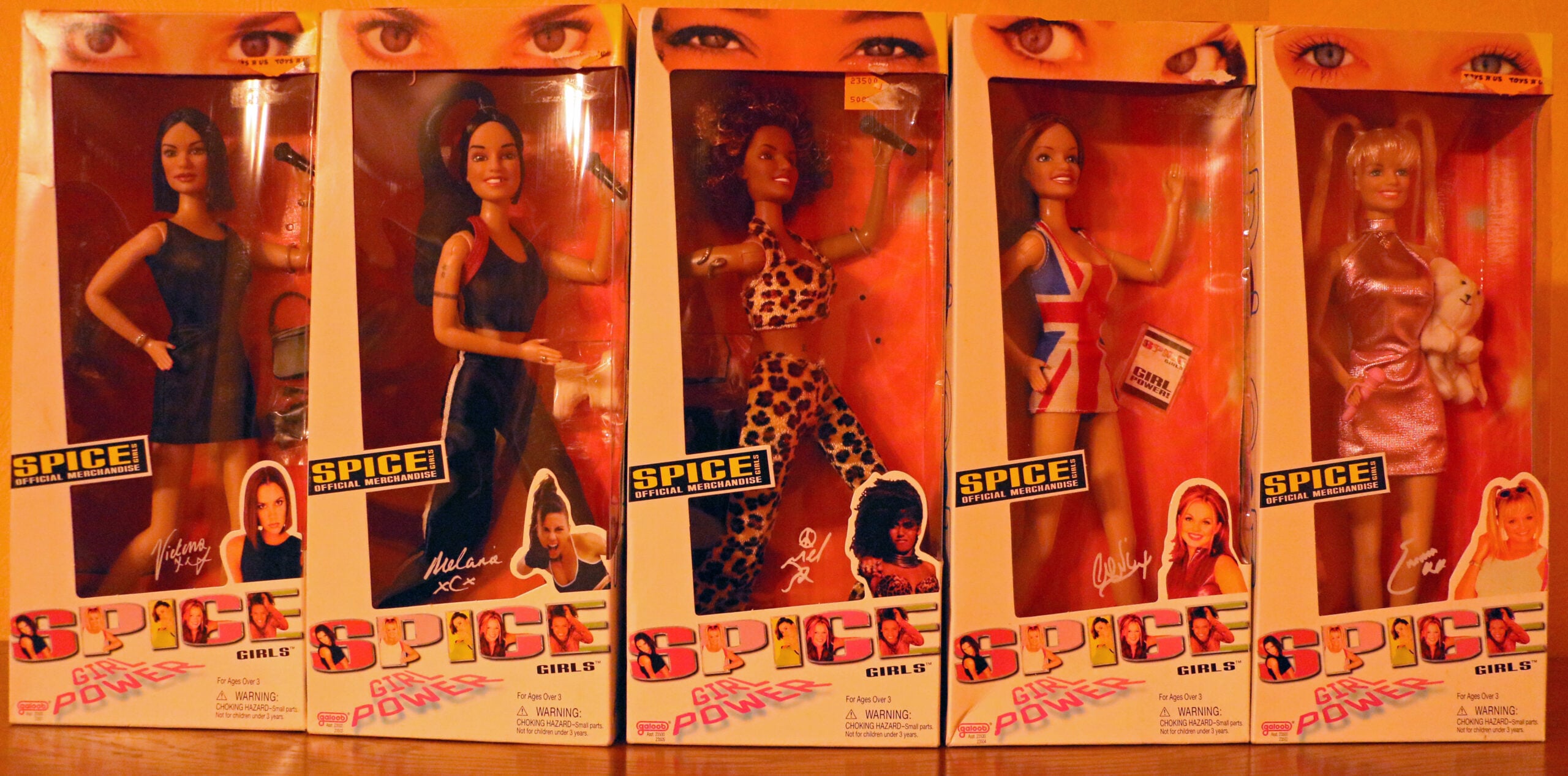 Five boxed Spice Girls dolls, each in themed outfits representing the band members. The boxes are orange with images of the bandmates’ faces and signatures, and display the words “SPICE GIRL POWER.”