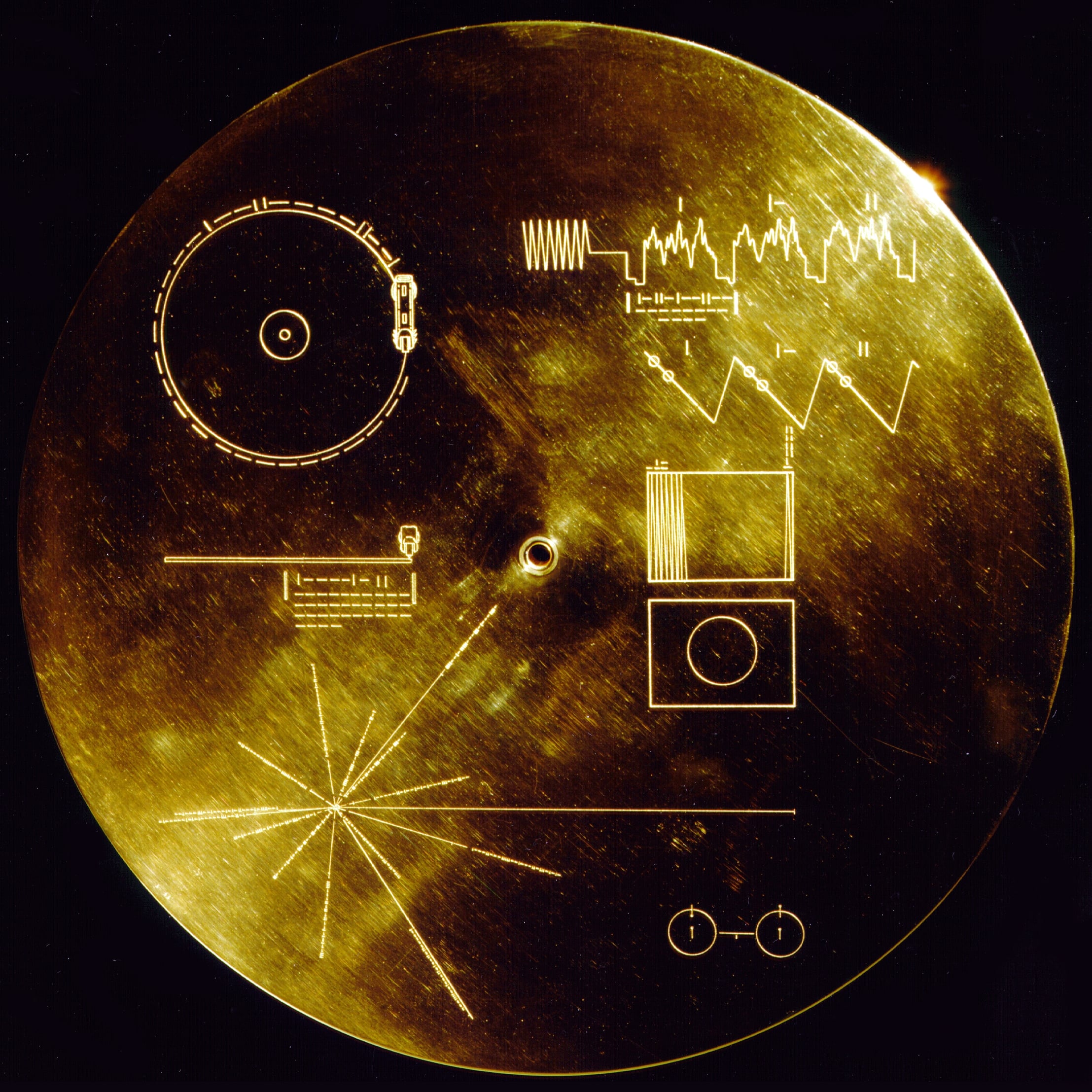 A gold disc with engraved scientific diagrams, waveforms, a star map, and a record player illustration; known as the Voyager Golden Record.