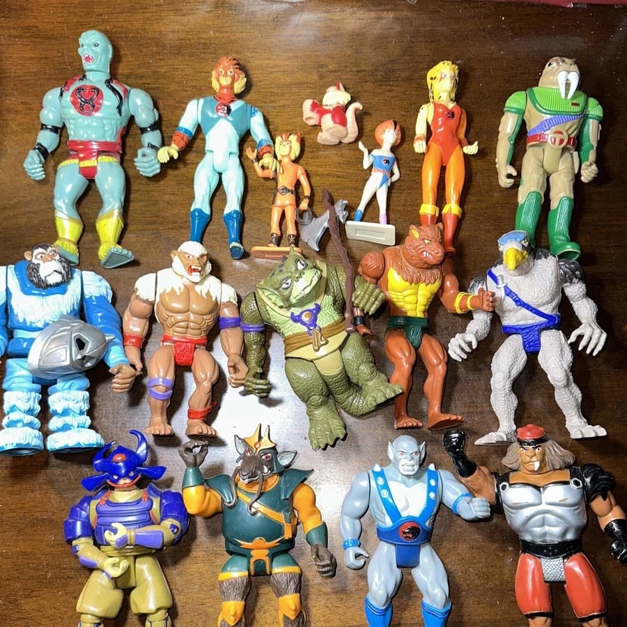 A collection of Thundercats action figures, including heroes and villains, arranged on a wooden surface. The figures are colorful and detailed, representing various characters from the animated series.
