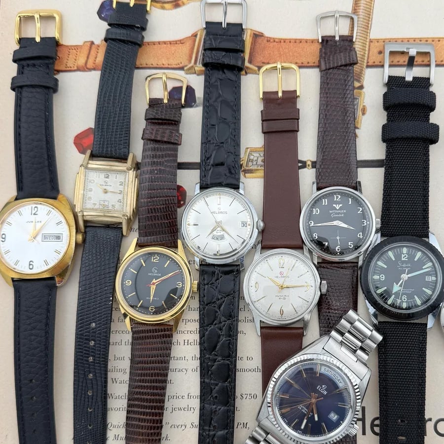 Eight assorted wristwatches with various bands and faces are arranged side by side on a printed background featuring text and vintage illustrations.