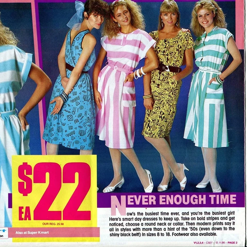 Four women in bright, patterned 1980s dresses stand smiling with hands on hips. A large yellow price sign reads “$22 EA.” Text below advertises dresses. The background is a solid blue color.