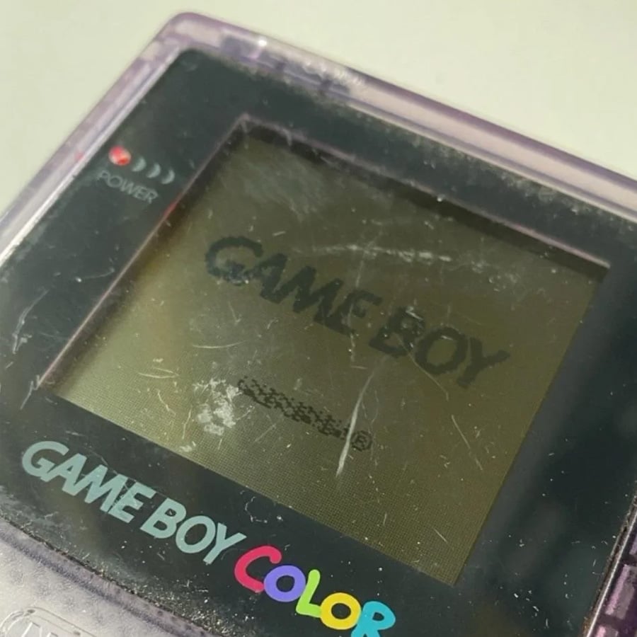 Close-up of a scratched, translucent purple Game Boy Color showing the “GAME BOY” logo on its screen.