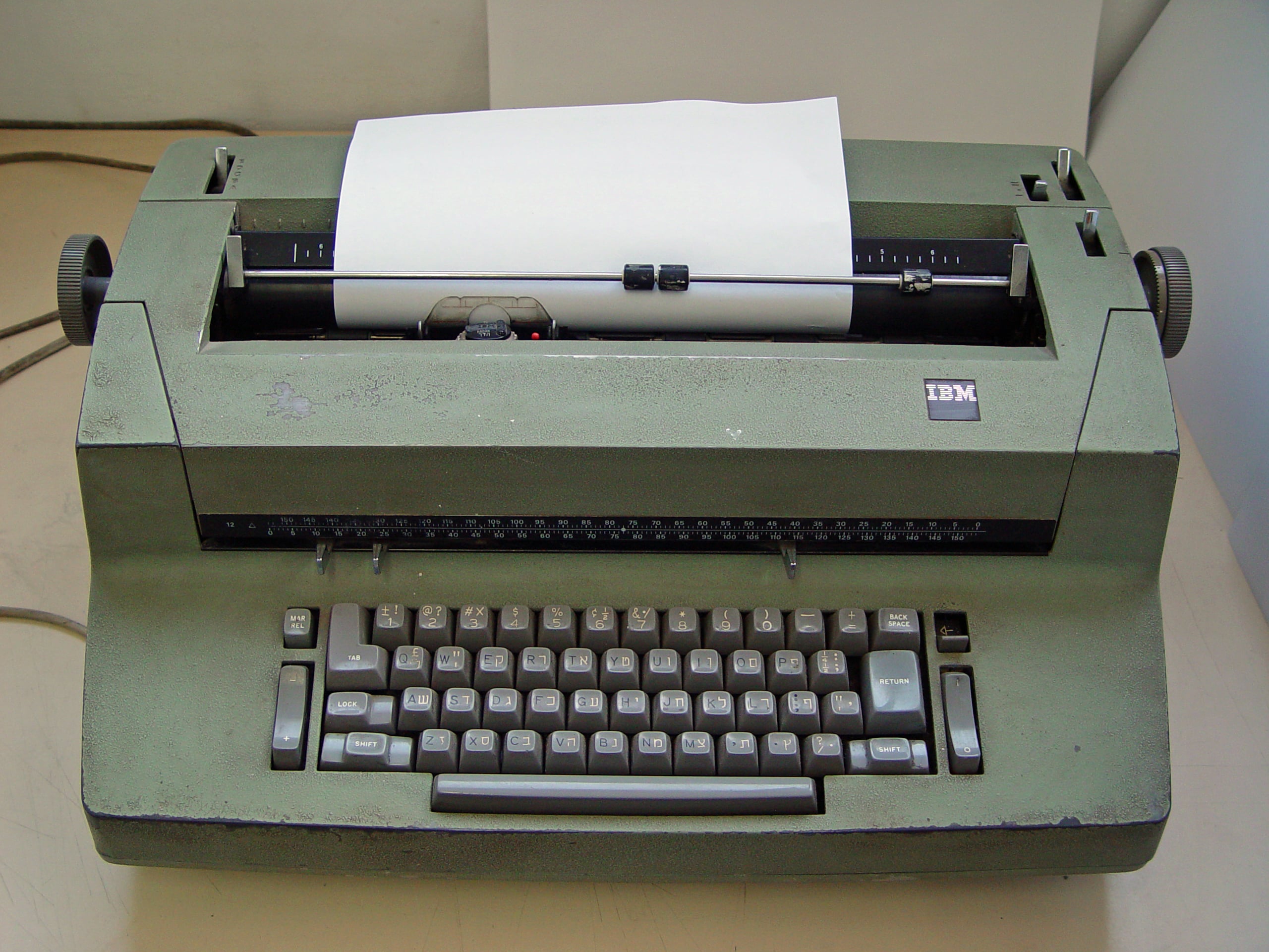 A vintage green IBM typewriter with a sheet of paper loaded, viewed from above, showing its keyboard and mechanisms.