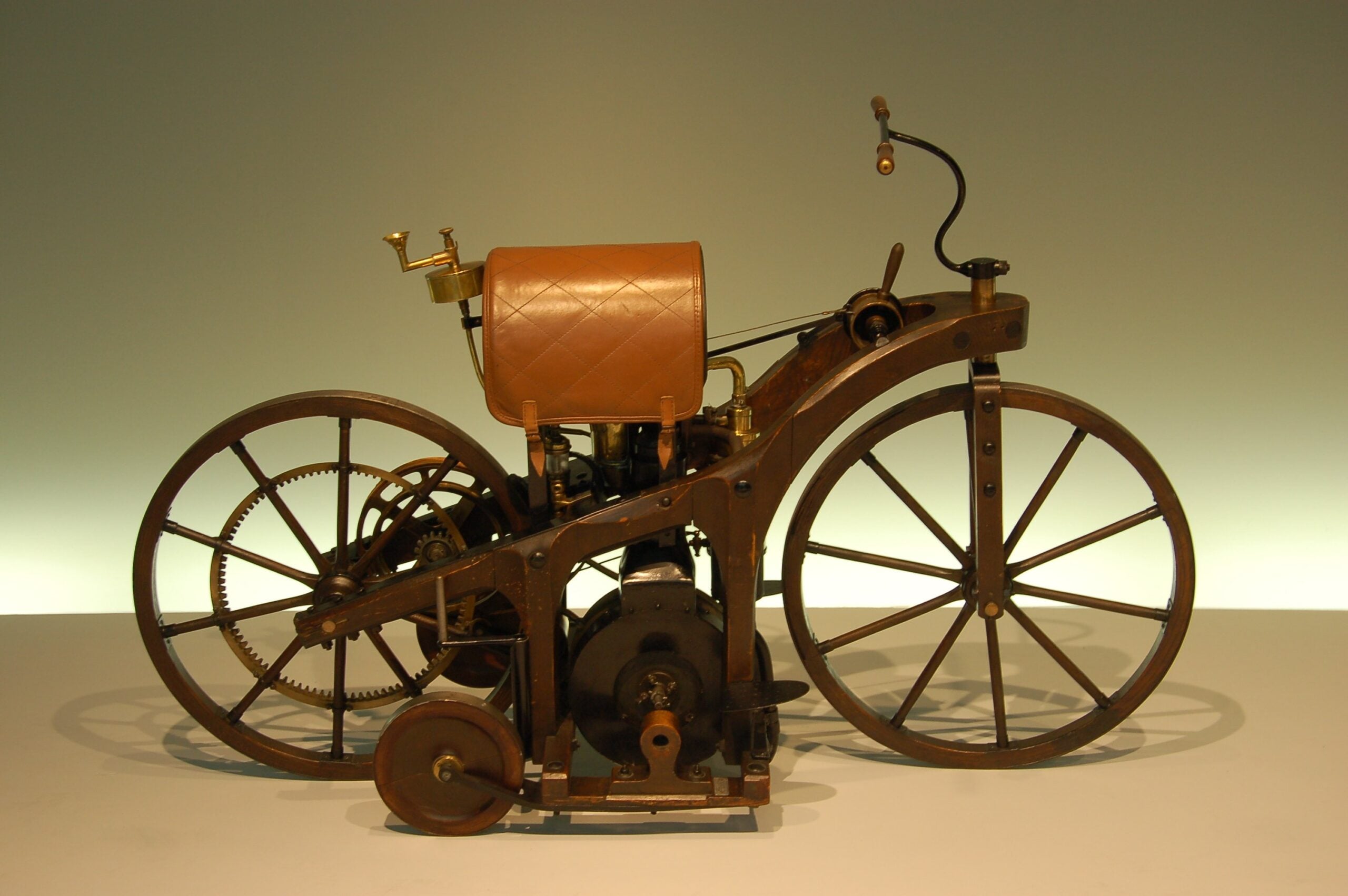 A vintage wooden motorcycle with large spoked wheels, a leather seat, and an exposed engine, displayed on a plain background.