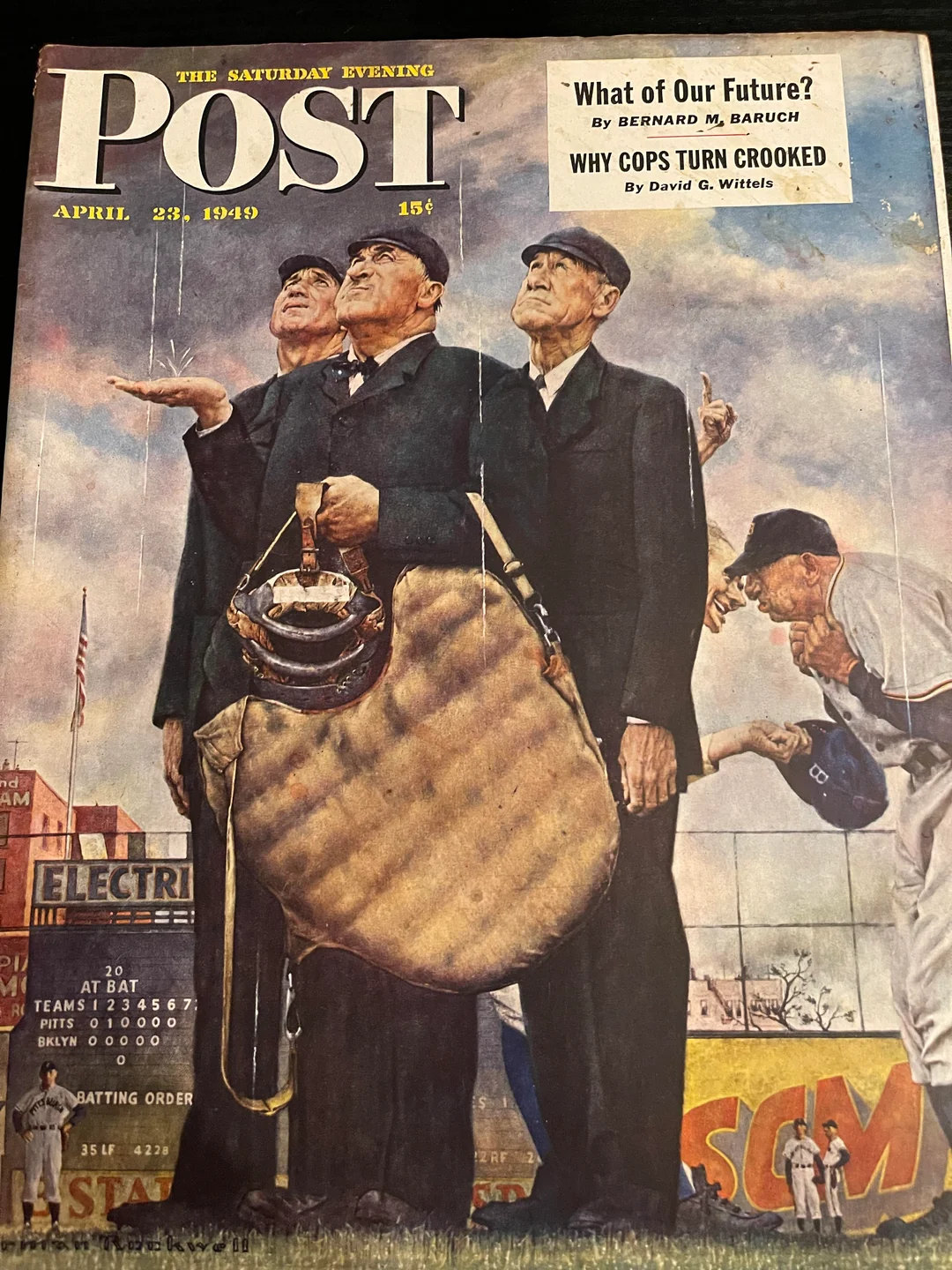 Three baseball umpires look up at a cloudy sky, unsure if the game will continue. Players and a crowded stadium are visible in the background. The magazine cover is dated April 23, 1949.