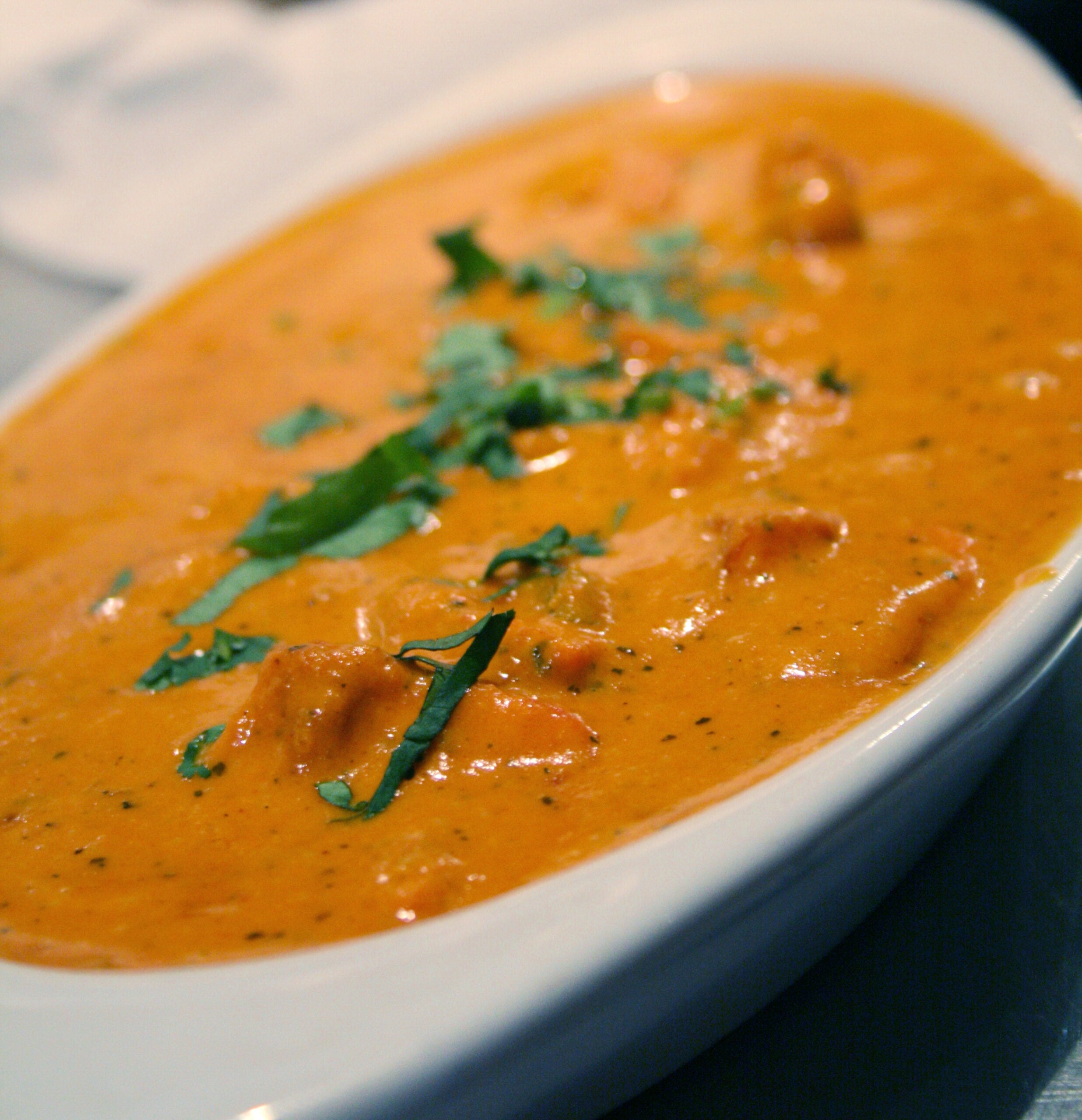 A close-up of a creamy orange curry, garnished with fresh cilantro, served in a white oval dish.