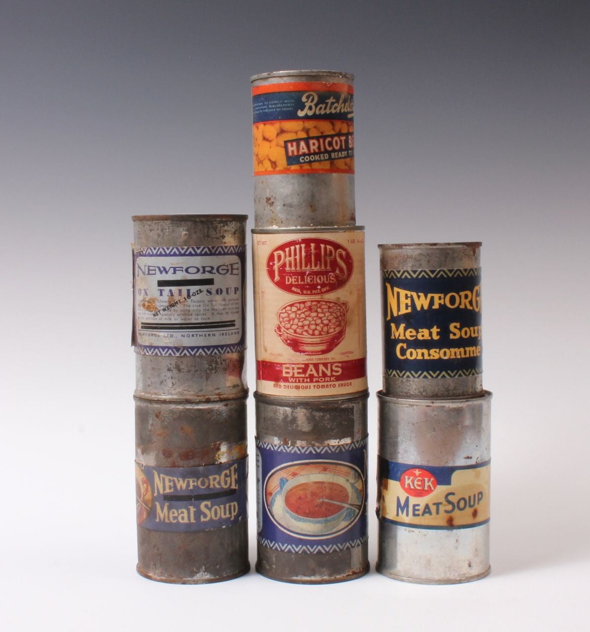 Six vintage canned food tins, including beans, oxtail soup, haricot beans, and meat soup, arranged in a pyramid on a neutral background. The labels are colorful but the cans appear old and rusty.