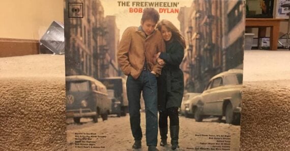 Vinyl record cover of “The Freewheelin’ Bob Dylan” showing a man and woman walking close together on a city street, with parked cars and buildings in the background.