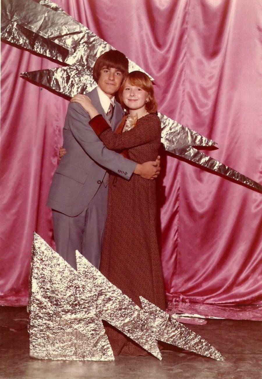 Two teenagers in formal clothes pose together in front of pink satin curtains with large, silver, lightning bolt decorations.