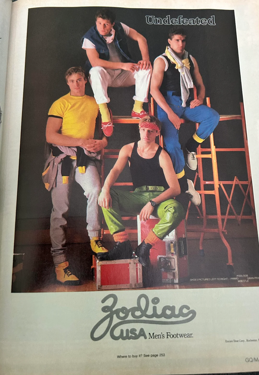 Four men pose in colorful 1980s athletic wear and sneakers, standing and sitting on gym equipment. “Undefeated” appears above them. The ad is for Zodiac USA Men’s Footwear.