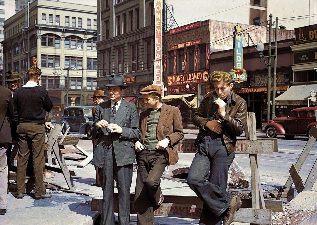 Three men in 1930s-style clothing stand by a construction barrier on a city street. Old cars and storefronts, including a “Money Loaned” sign, are visible in the background. The scene has a vintage, historical feel.
