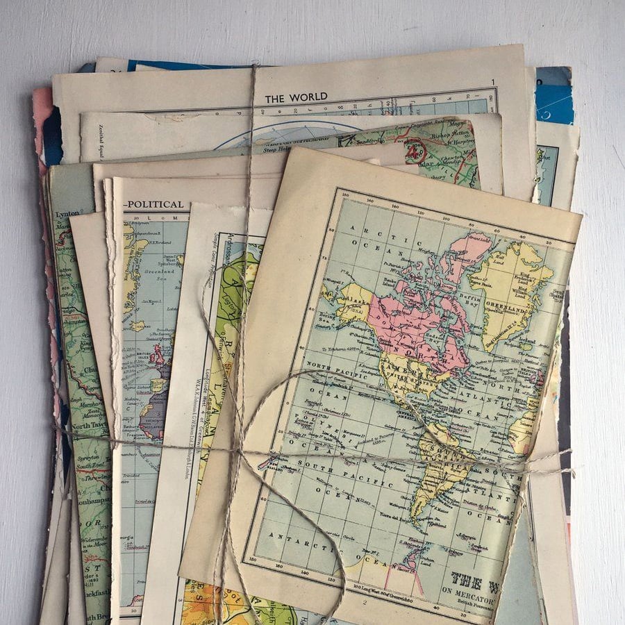 A stack of vintage maps tied with twine, showing colorful world and continent maps with visible borders and place names, placed on a light surface.