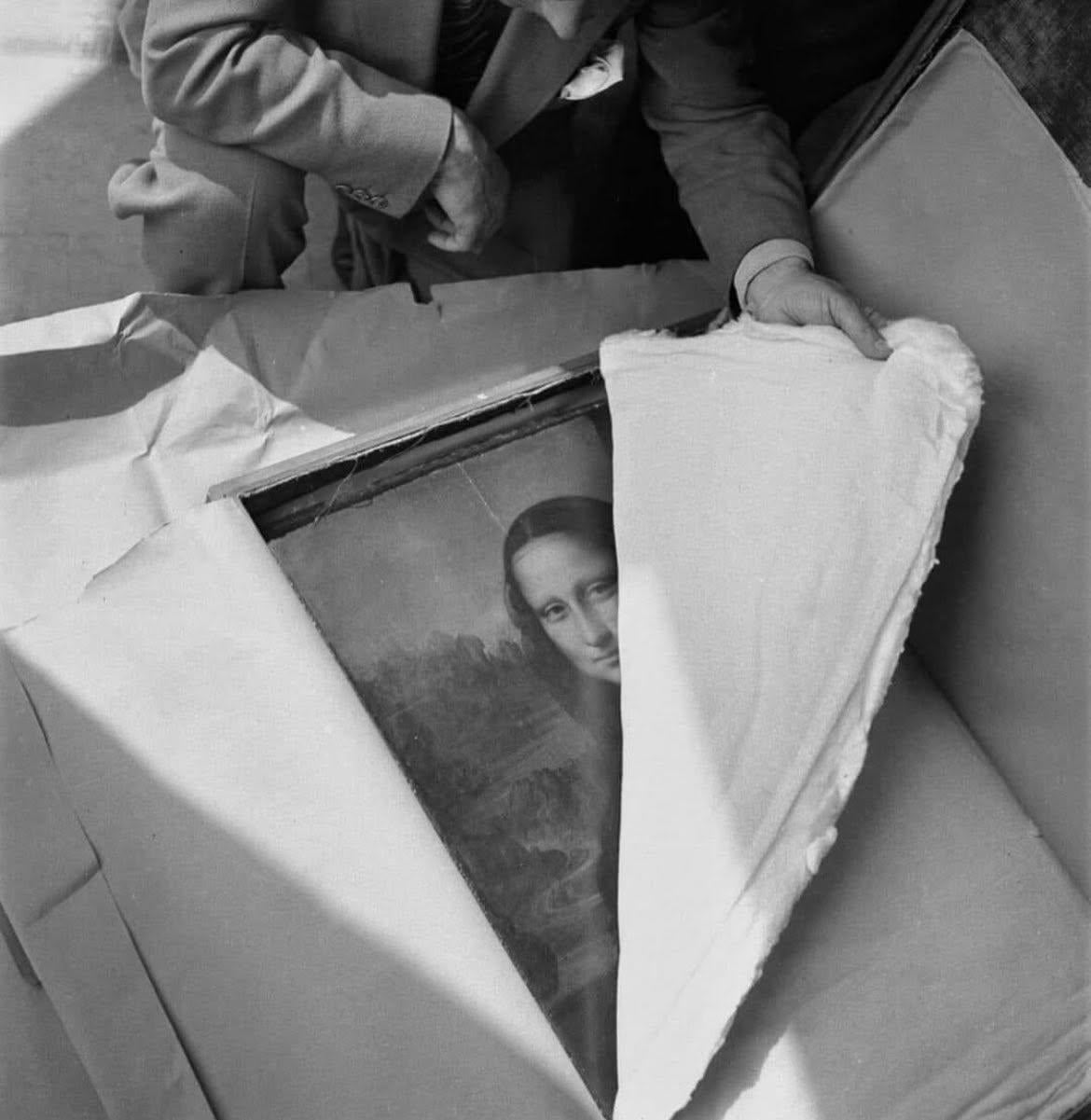 A person unwraps a framed painting partially covered by protective material, revealing the face of the Mona Lisa.