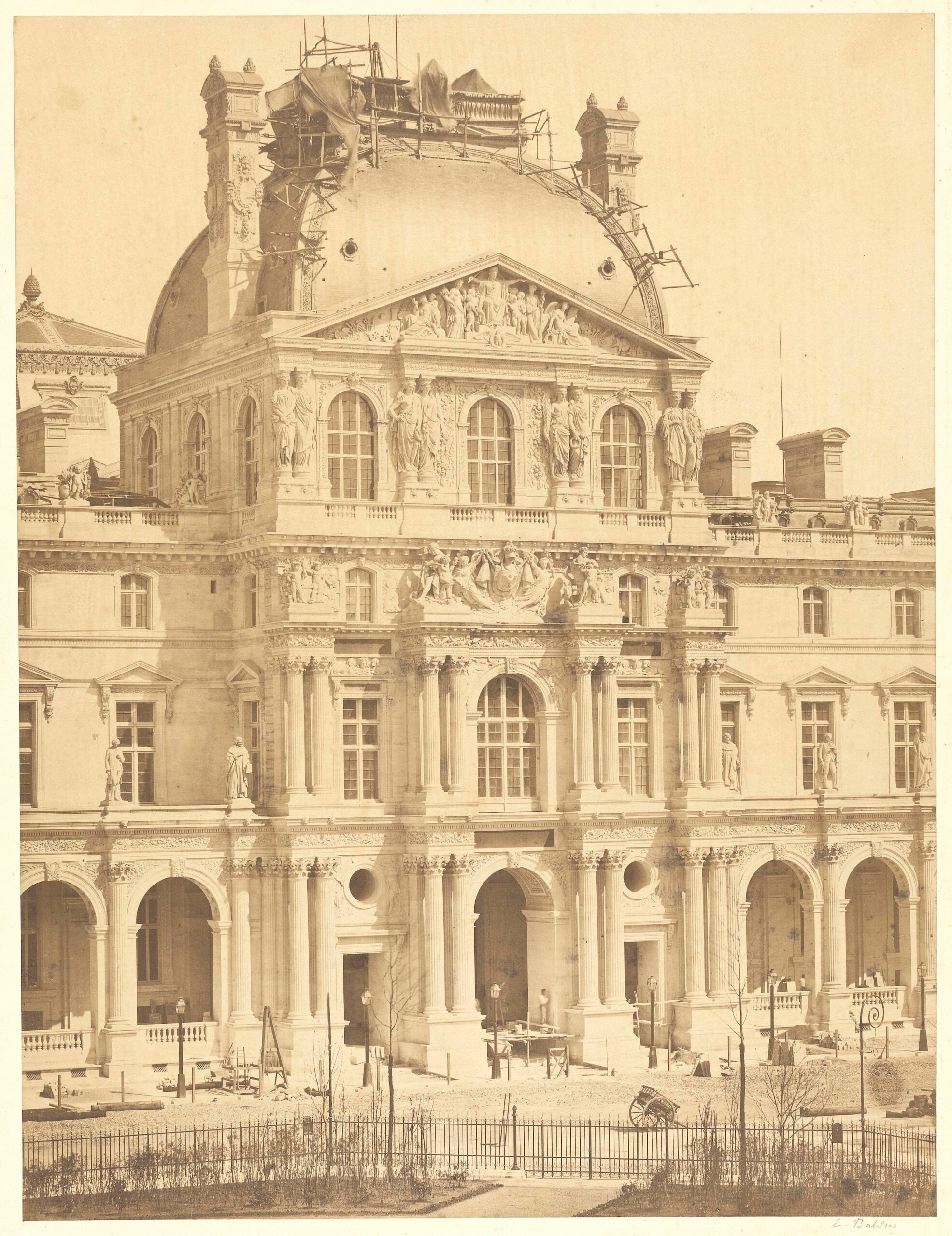 Sepia-toned photo of an ornate, domed building under construction, featuring columns, arches, balconies, and statues. Scaffolding is visible atop the dome. A wrought iron fence borders the foreground.