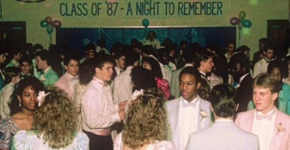 Crowd of teens in pastel dresses and tuxedos dance at a decorated prom. A banner reads “Class of ’87 - A Night to Remember.” Balloons and streamers are visible in the background.