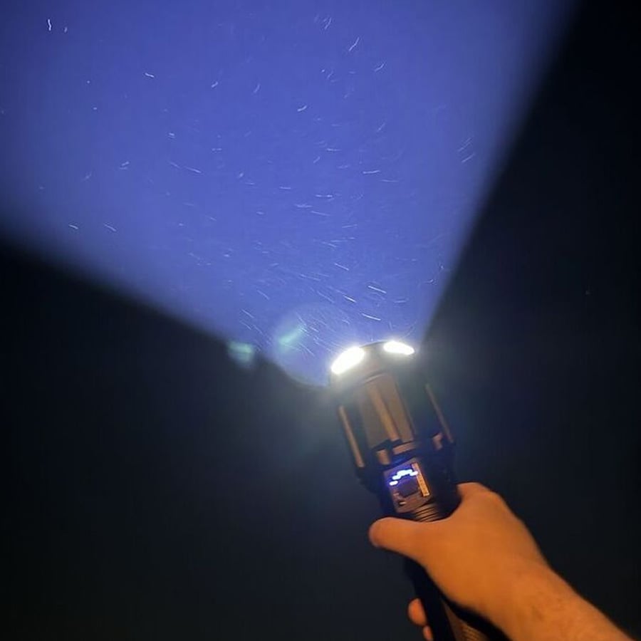 A hand holds a flashlight in the dark, casting a wide blue beam and illuminating dust or particles in the air.