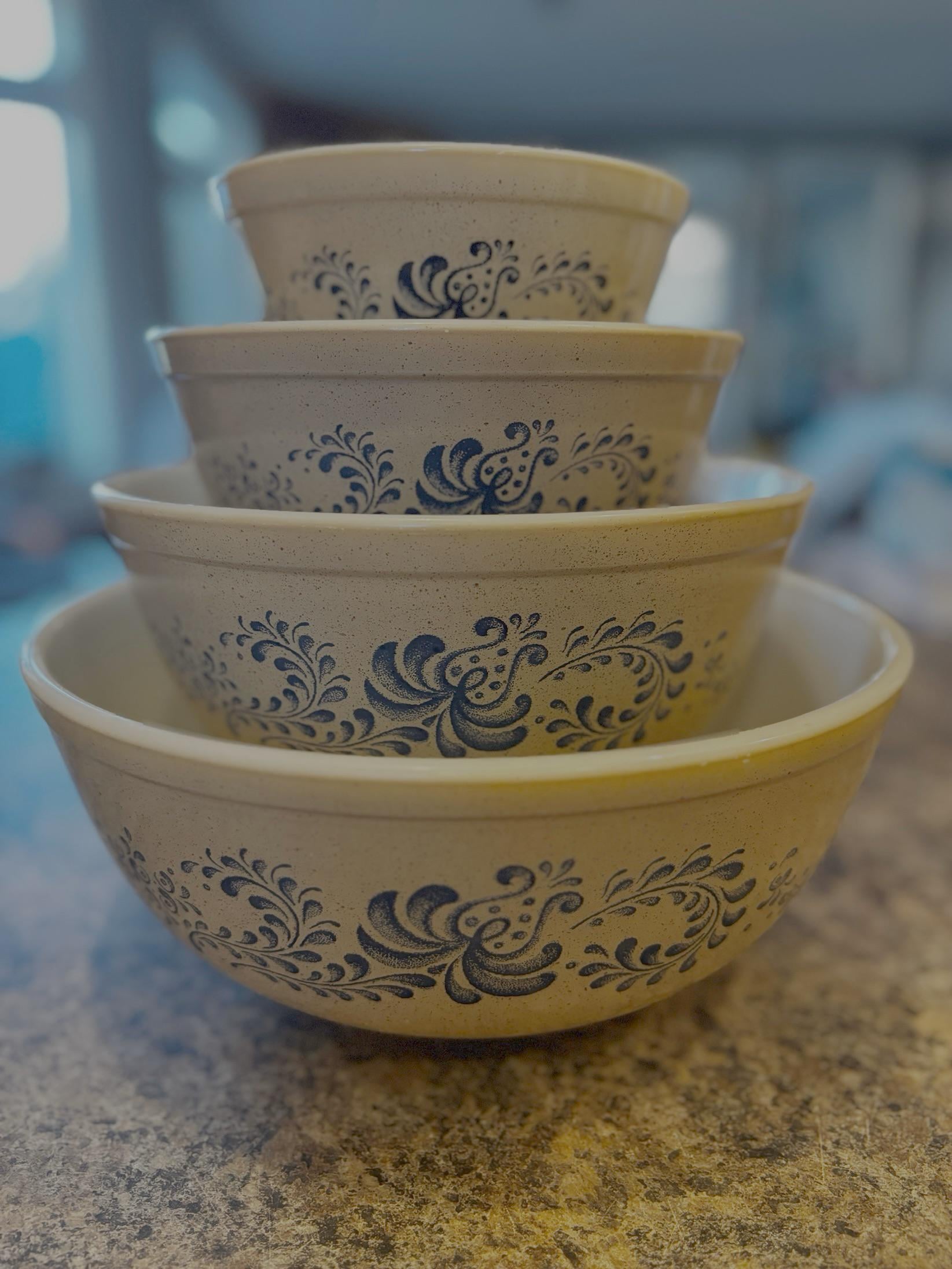 Four cream-colored mixing bowls with blue floral patterns are stacked inside each other on a countertop, with a softly blurred kitchen background.