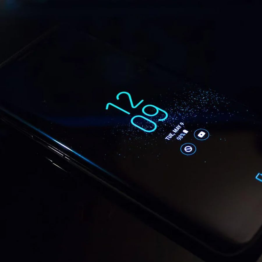 A smartphone displaying the time 12:09 and battery status on its screen, lying on a dark surface with a minimal, blue glowing interface.