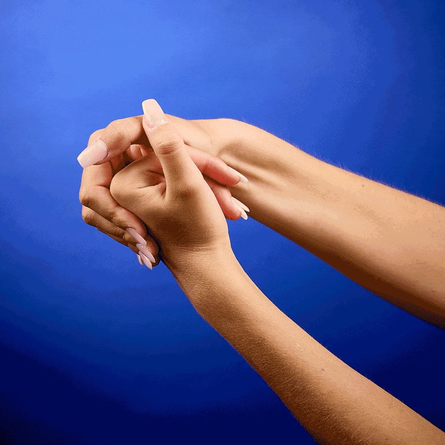 Two hands with manicured nails are clasped together against a solid blue background.