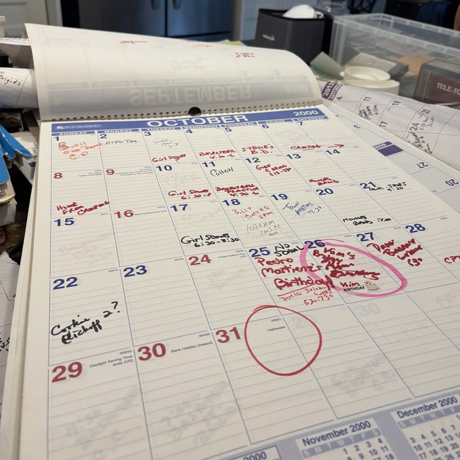 A close-up of an open planner showing October 2000, filled with handwritten notes and events in red and black ink. Other items and papers are scattered around the planner.