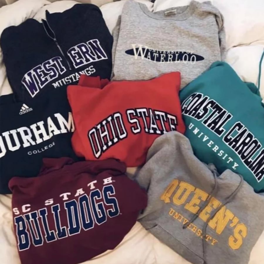 Six university sweatshirts arranged on a bed. Schools shown: Western, Waterloo, Durham, Ohio State, Coastal Carolina, SC State Bulldogs, and Queen’s University.