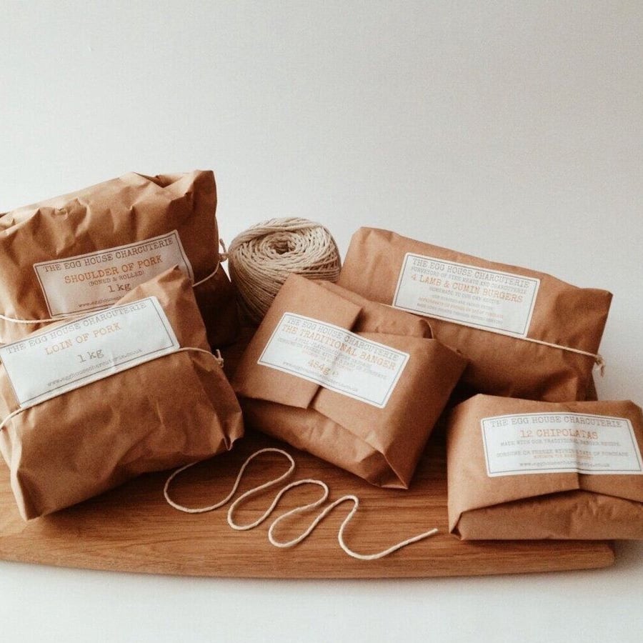 Five brown paper-wrapped packages of meat with white labels sit on a wooden board, beside a ball of twine and a loose piece of string. The parcels are neatly arranged and labeled with their contents.