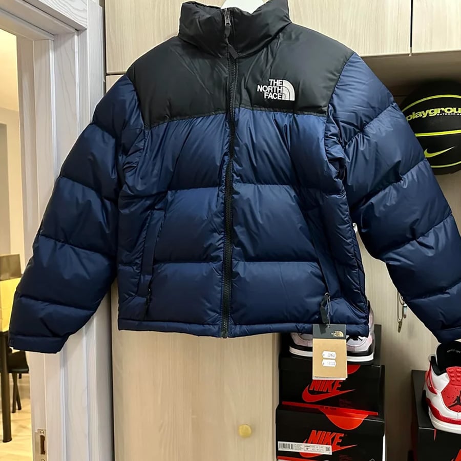 A blue and black North Face puffer jacket hangs on a closet door above stacked Nike shoe boxes, with tags still attached.