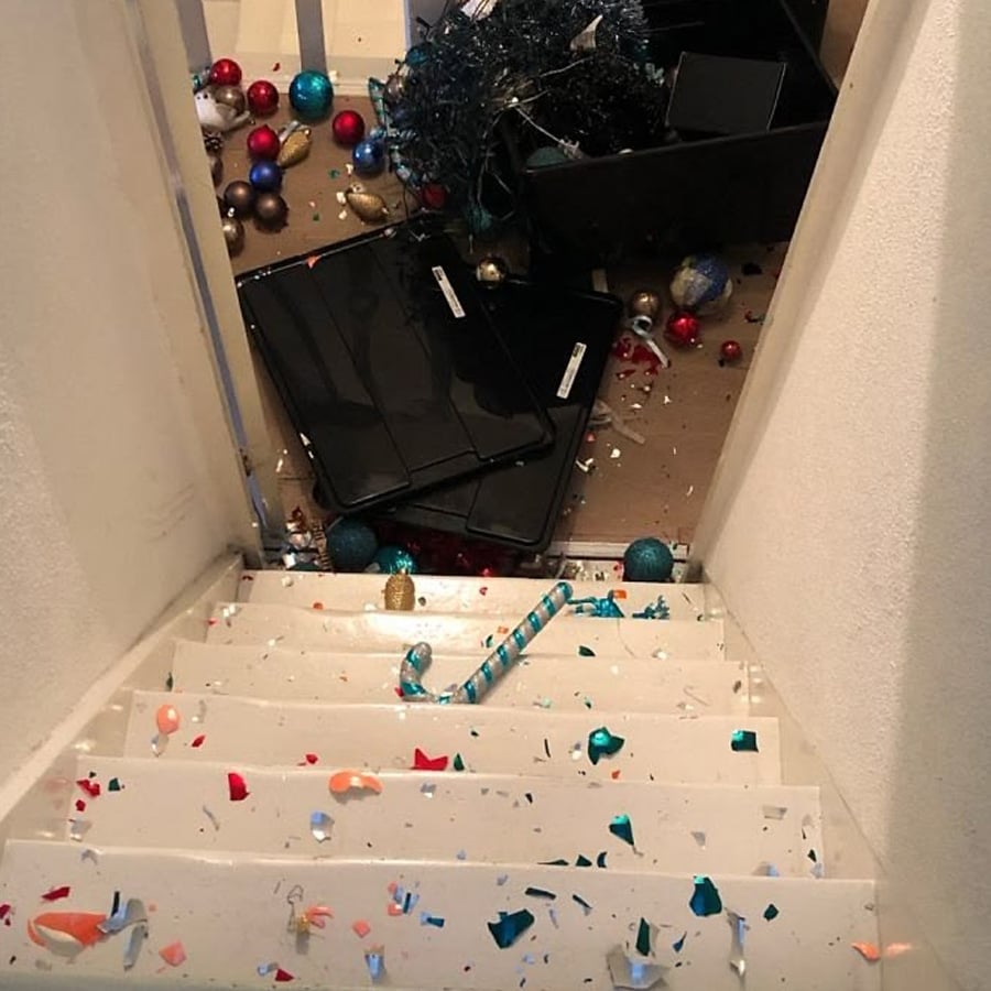 Shattered Christmas ornaments, decorations, and broken shards are scattered down a white staircase and at the bottom, creating a colorful, chaotic mess.
