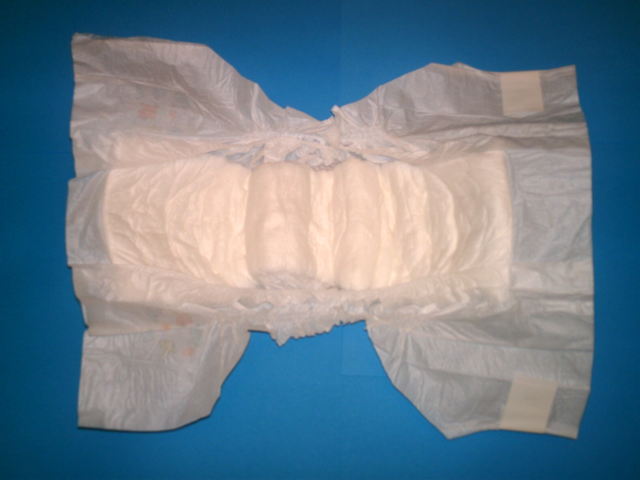 A disposable diaper is spread open on a blue background, showing its absorbent inner padding and side tabs.