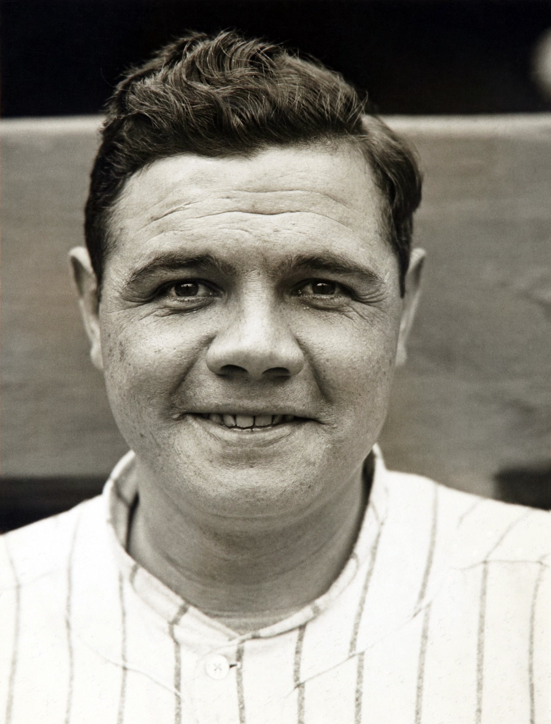 A man with short dark hair, wearing a striped baseball jersey, smiles slightly at the camera. The background is out of focus.