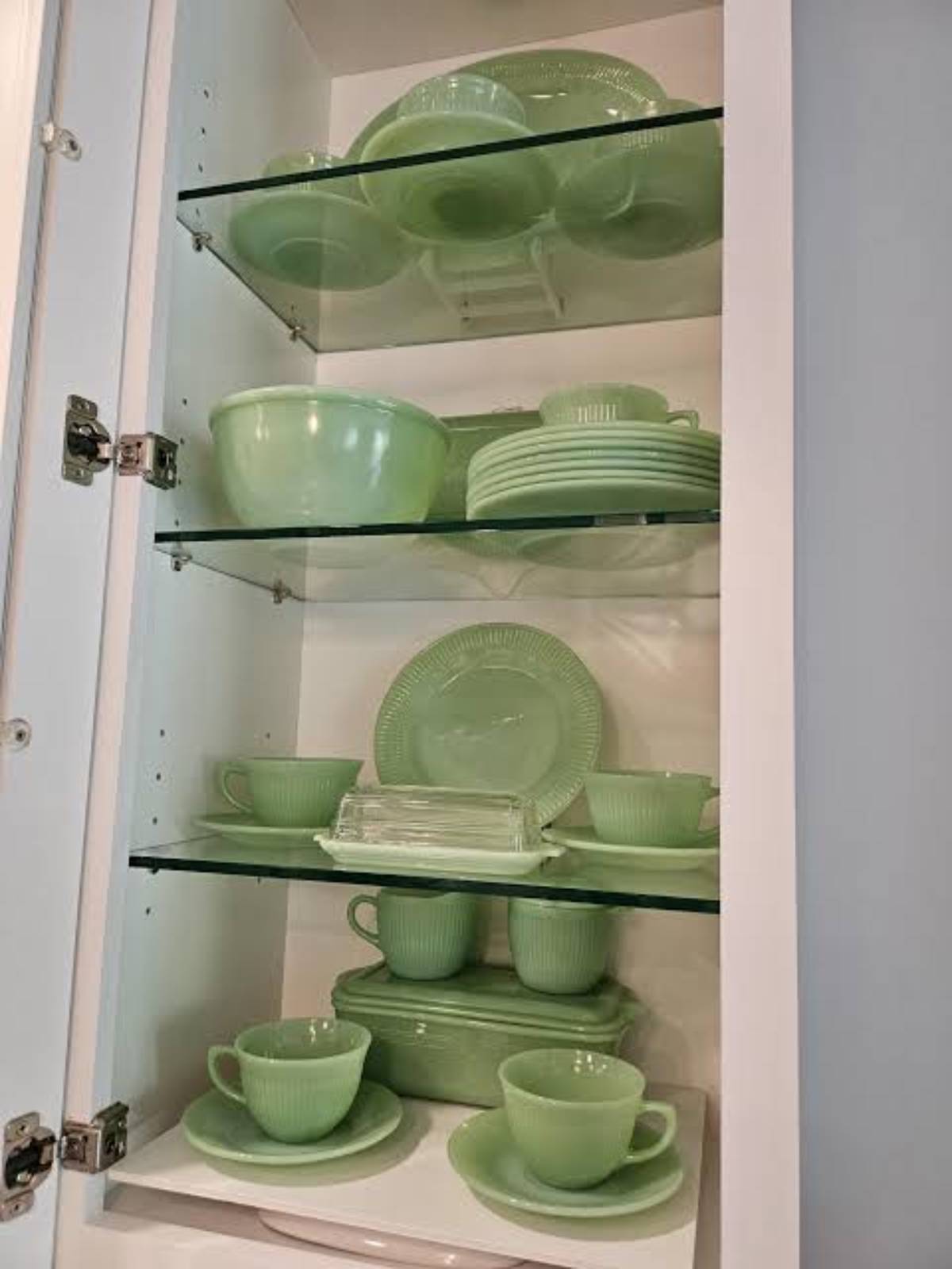 A cabinet with three glass shelves displaying green glass dinnerware, including cups, saucers, bowls, and plates, all neatly arranged.