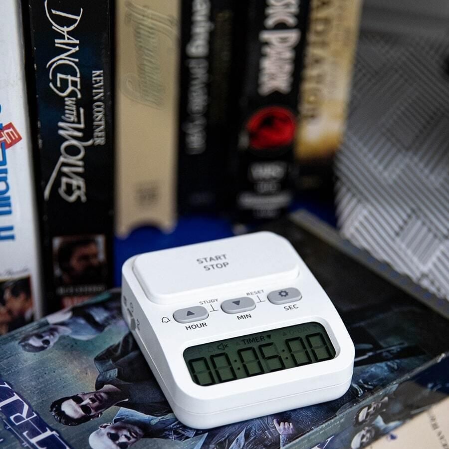 A white digital timer set to 15 minutes sits on top of a Game of Thrones DVD box, with several vertically stacked movie DVDs in the background.