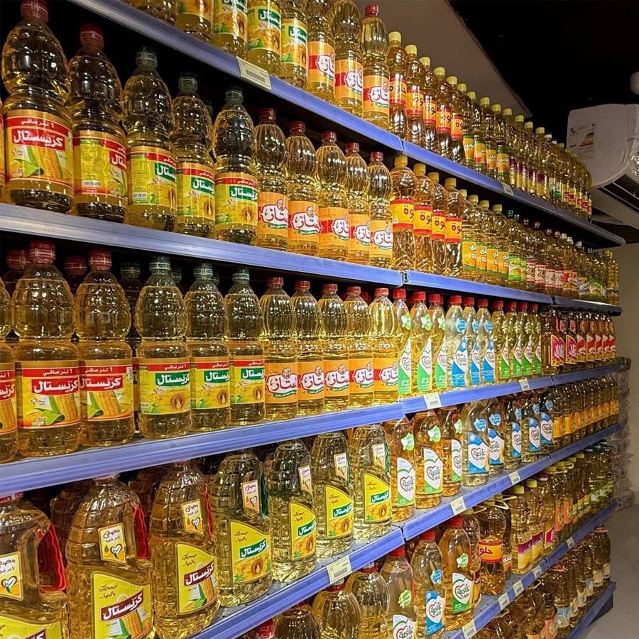 Bottles of cooking oil in various brands and colors are neatly arranged on multiple shelves in a grocery store aisle.