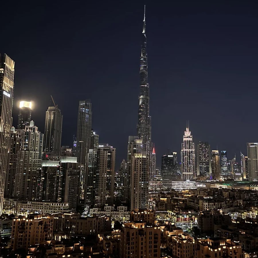 A nighttime cityscape featuring the illuminated Burj Khalifa surrounded by other high-rise buildings and city lights in downtown Dubai.