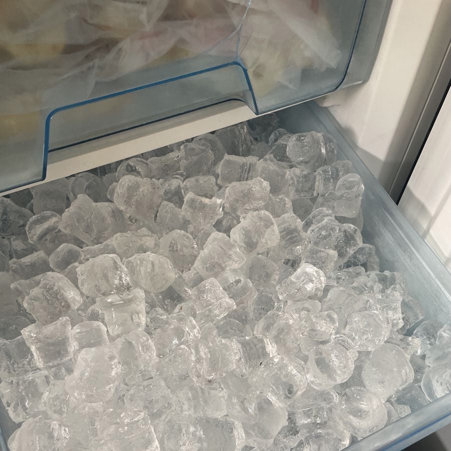 A drawer-style freezer compartment filled with clear, cube-shaped ice cubes. Some condensation is visible on the plastic surfaces inside the freezer.