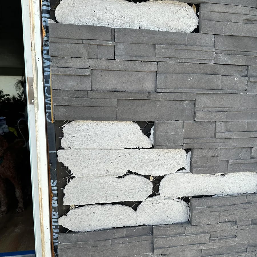 A partially finished wall with gray stone veneer and visible patches of white mortar, showing an incomplete section near a doorway.