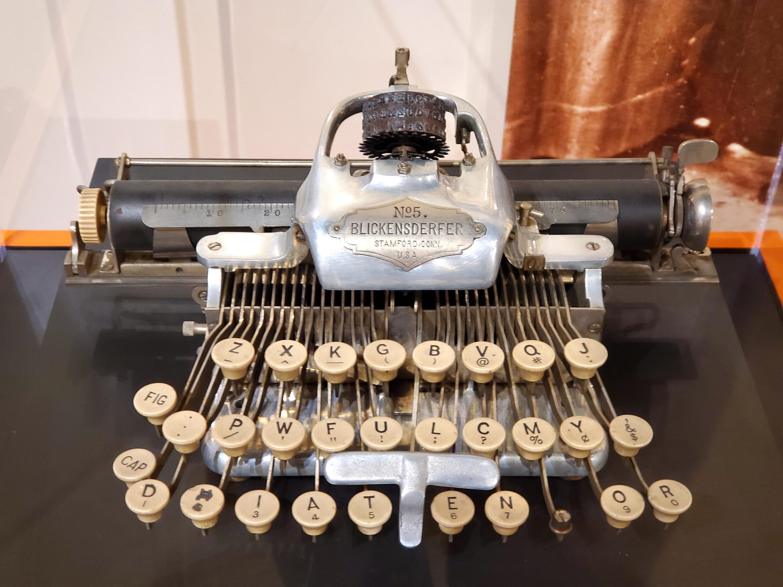 An antique Blickensderfer No. 5 typewriter with round white keys, metal arms, and a cylindrical paper roller, displayed on a flat surface.