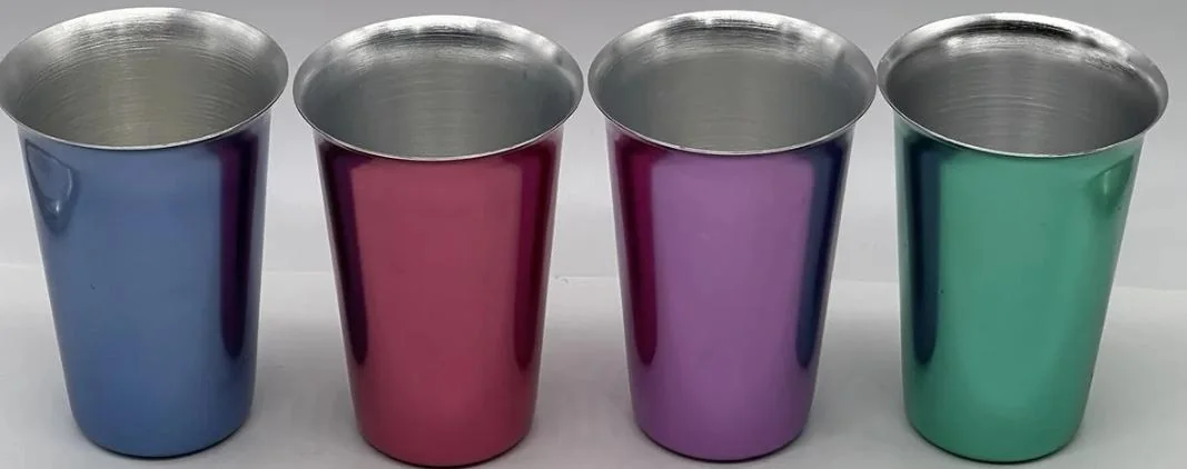 Four metallic cups in blue, red, purple, and green are lined up side by side on a white surface with a simple background.