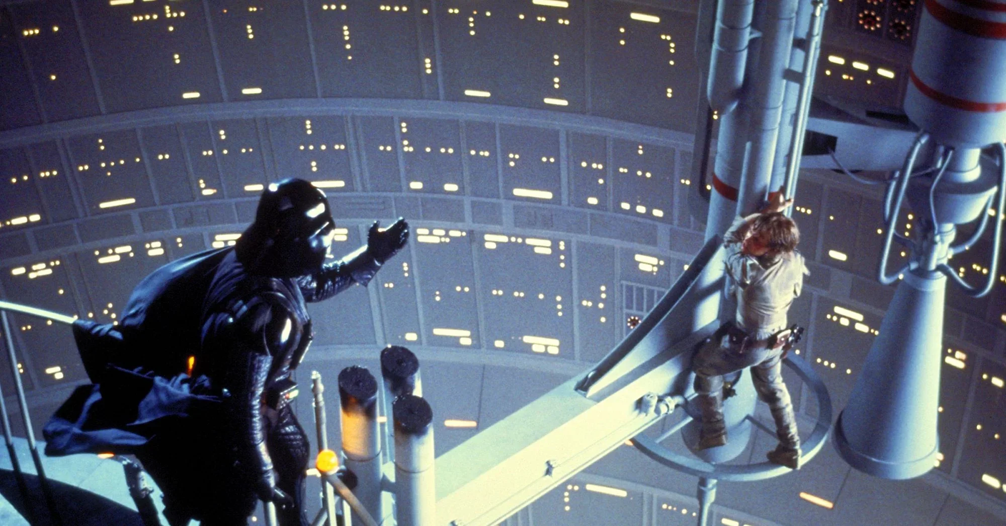 Darth Vader reaches out to Luke Skywalker, who clings to a narrow platform above a deep futuristic shaft filled with lights, in a dramatic scene from Star Wars.