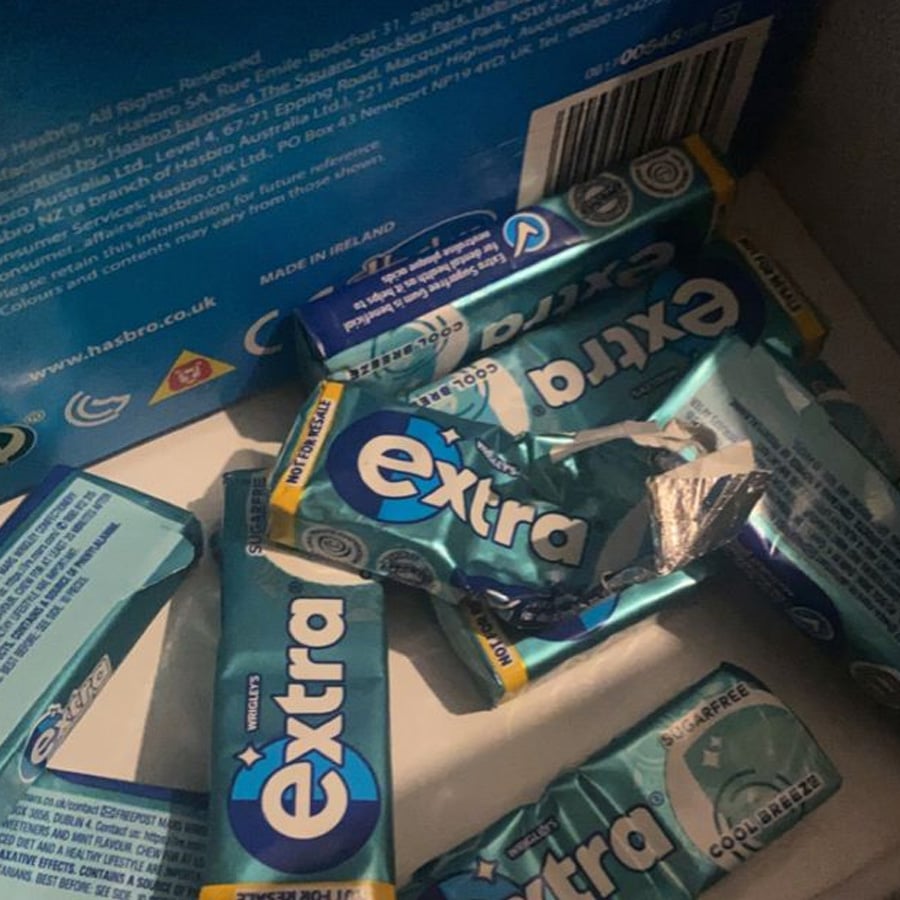 Several packs of Extra cold breeze chewing gum, some opened, are scattered inside a cardboard box. The packs are mostly blue with white and black text, and the box has blue printed details.