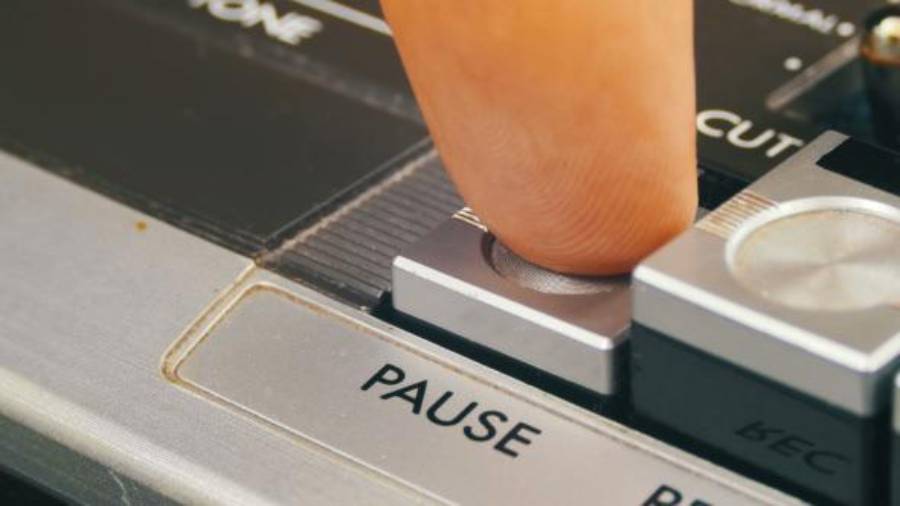A close-up of a finger pressing the pause button on a vintage audio cassette player, with “PAUSE” clearly labeled on the device.