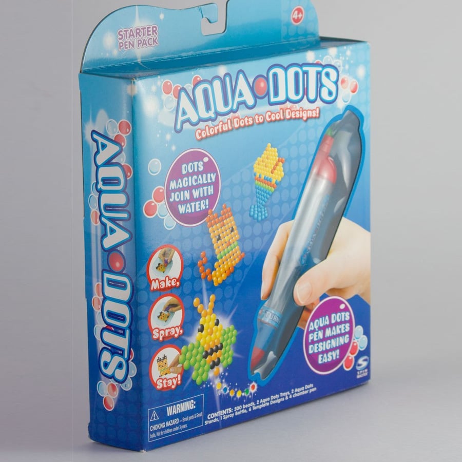 Aqua Dots starter pack box showing colorful dot designs and a hand holding the Aqua Dots pen. The box highlights how dots join with water and includes phrases like “Make, Spray, Stay!” and “Colorful Dots to Cool Designs!”