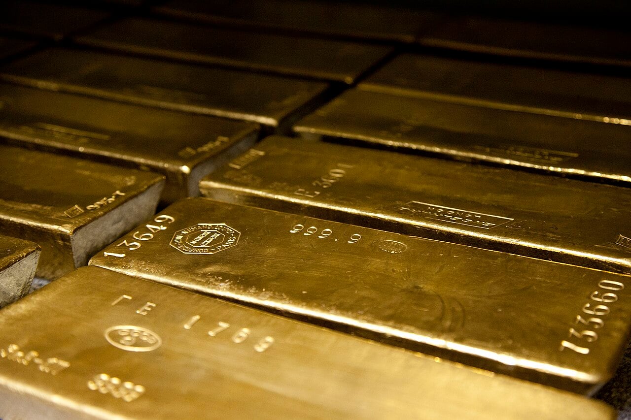 Stacks of shiny gold bars with serial numbers and markings, arranged closely together in a secure storage area.