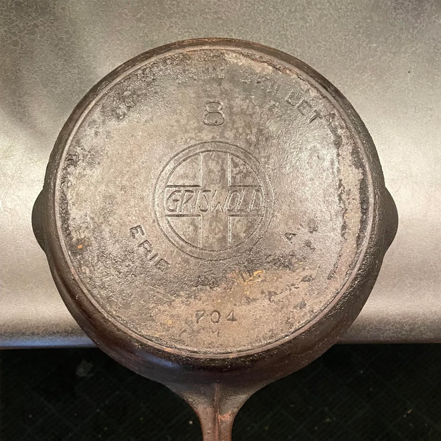 A vintage cast iron skillet with “Griswold,” “Erie PA, U.S.A.,” and the number “8” embossed on the bottom. The surface shows signs of wear and age.