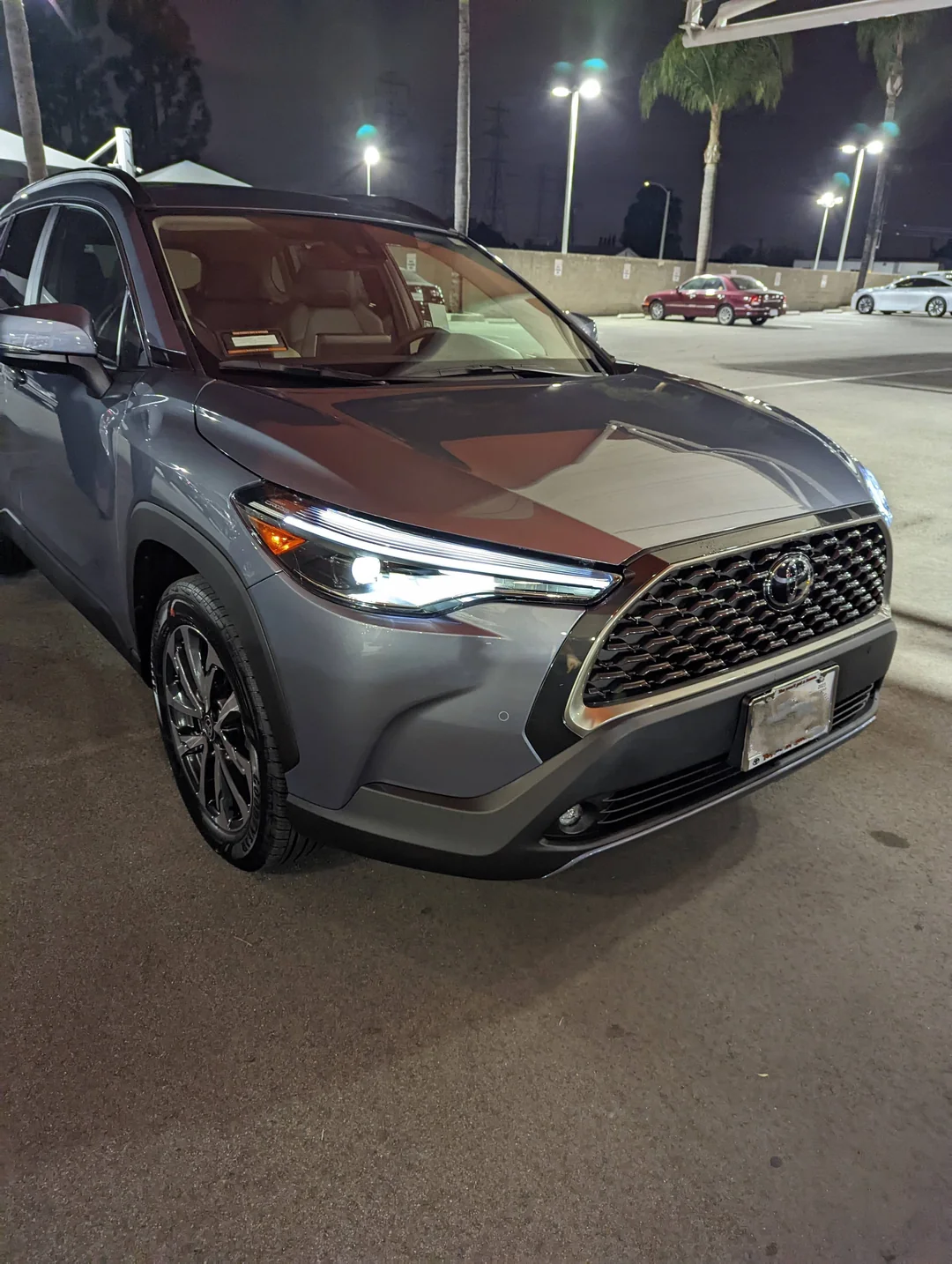A silver SUV with its headlights on is parked at a gas station at night. Palm trees and other cars are visible in the background.