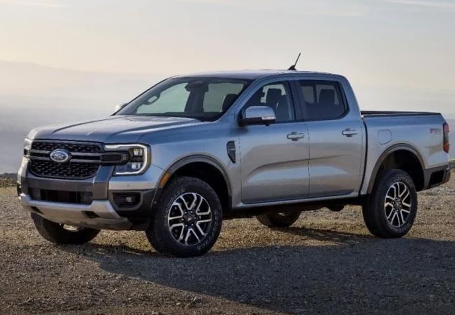 A silver pickup truck is parked outdoors on gravel, with a clear sky and landscape in the background.