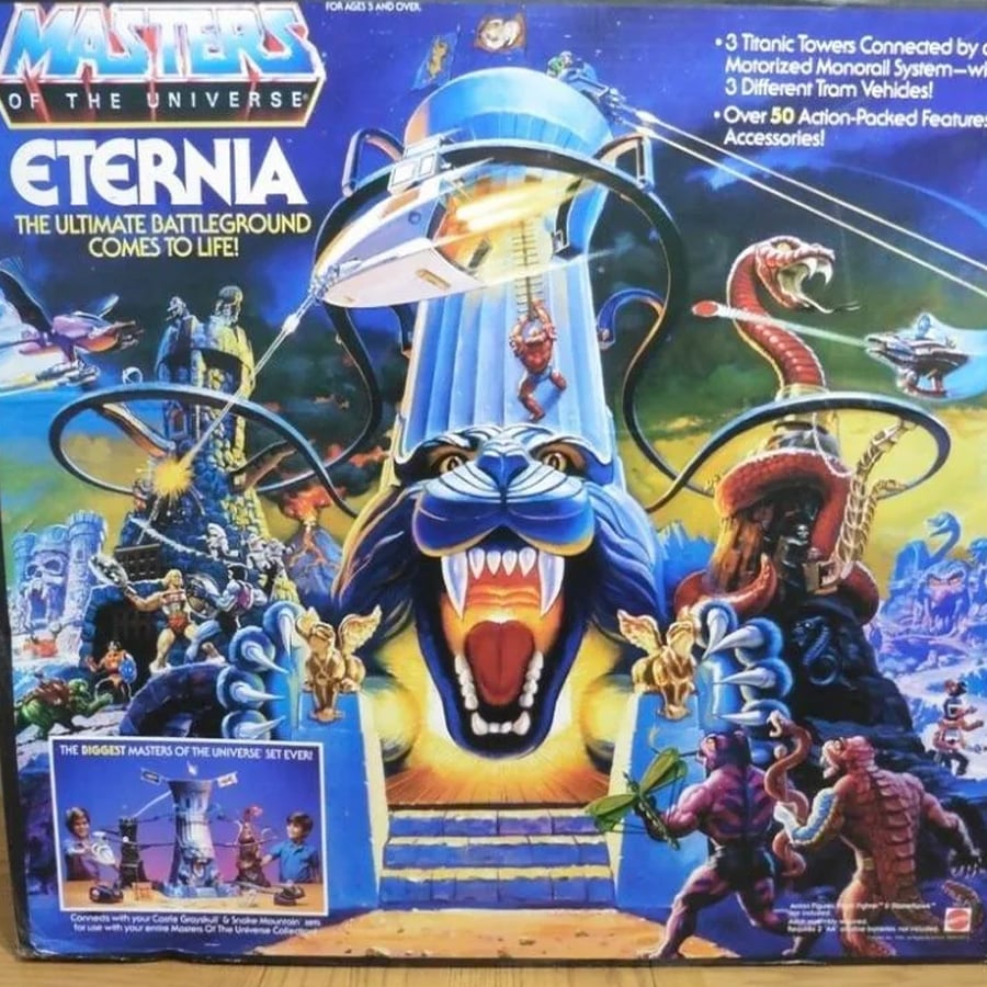 Box art for the Masters of the Universe Eternia playset, showing a fierce blue panther fortress, fantasy creatures, and warriors battling, with dramatic lightning and bright colors.