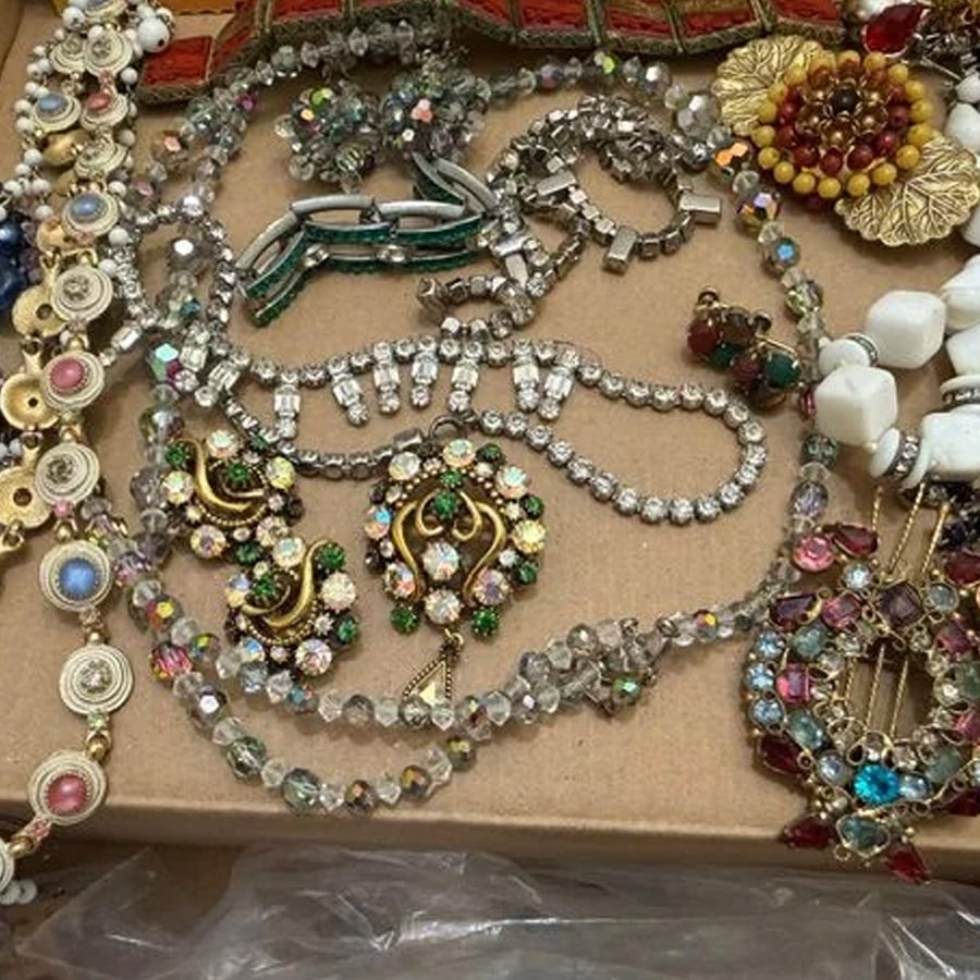 Various colorful necklaces, earrings, and bracelets with gemstones and beads are displayed on a cardboard surface, showcasing intricate designs and sparkling details.